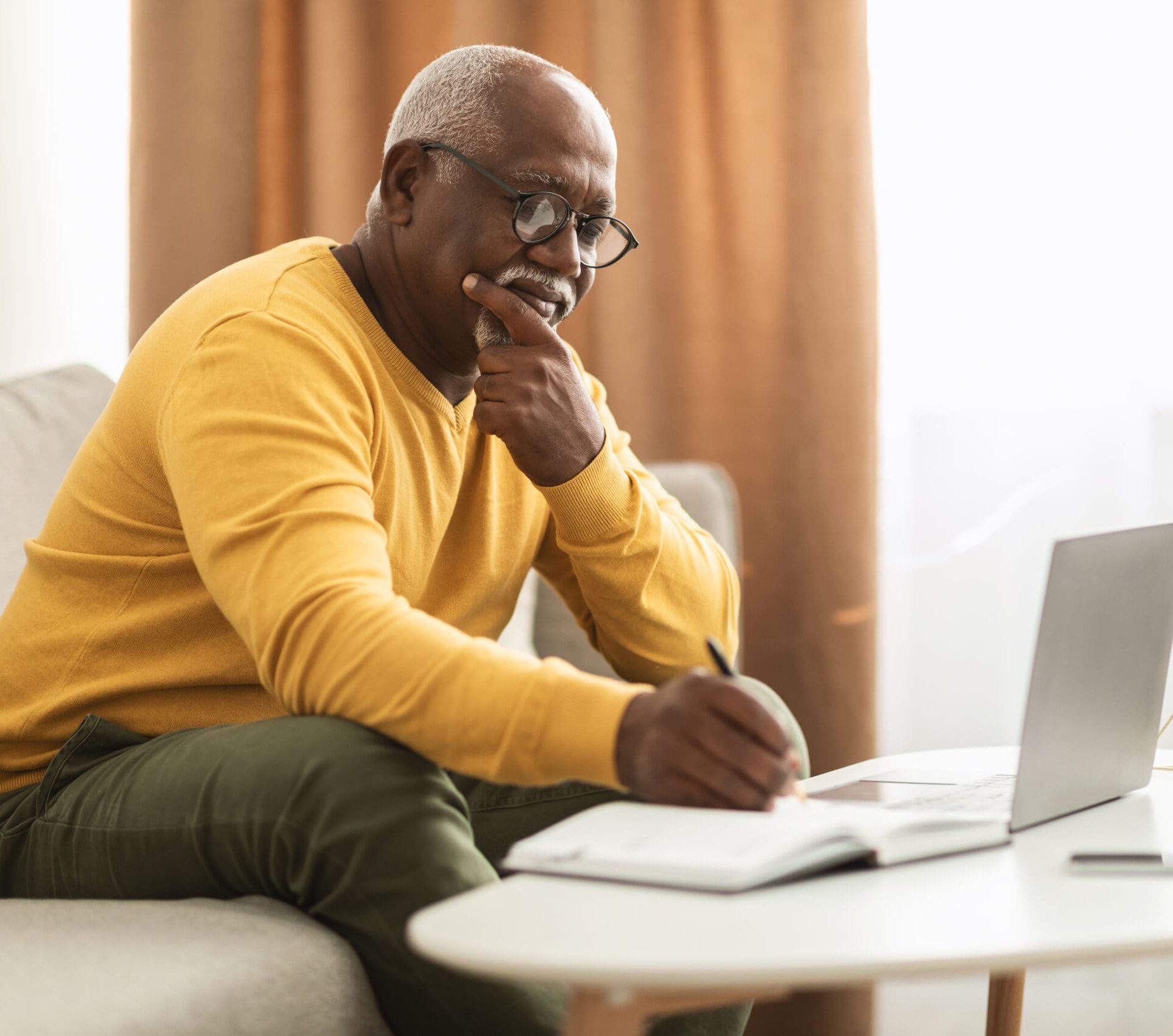 Mature Black Male Freelancer Using Laptop Taking Notes Working Indoors